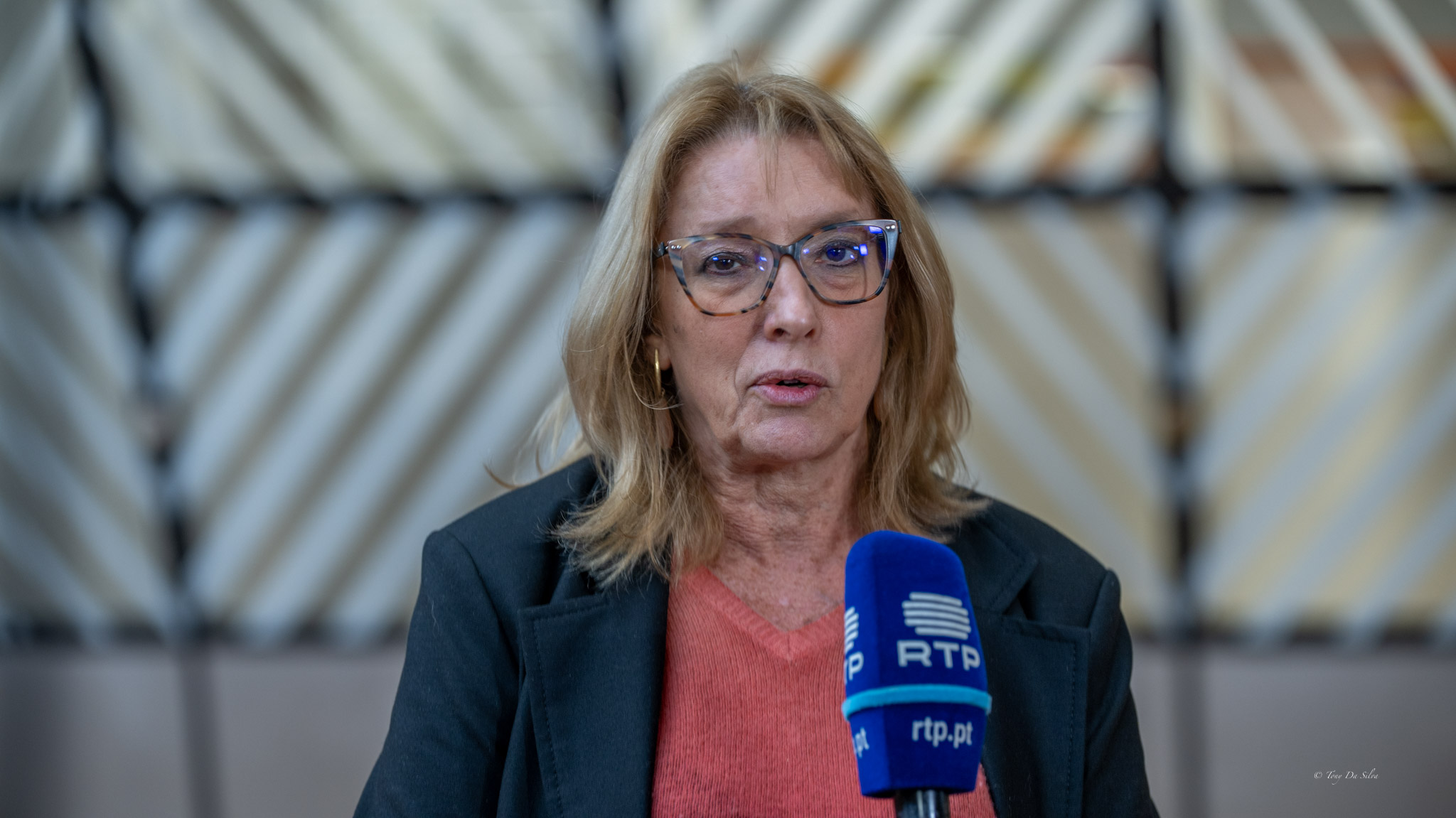 A ministra do Trabalho, Solidariedade e Segurança Social fala à imprensa em Bruxelas, com um microfone de televisão à sua frente, durante uma reunião ministerial da União Europeia.