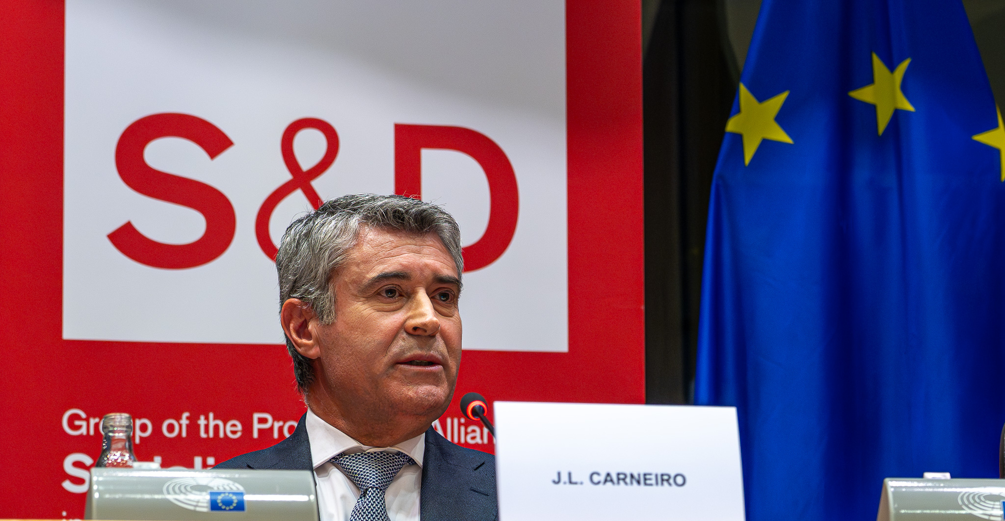 José Luís Carneiro, secretário-geral do PS, sentado numa cerimónia no Parlamento Europeu, com o logótipo do grupo S&D e a bandeira da União Europeia ao fundo.