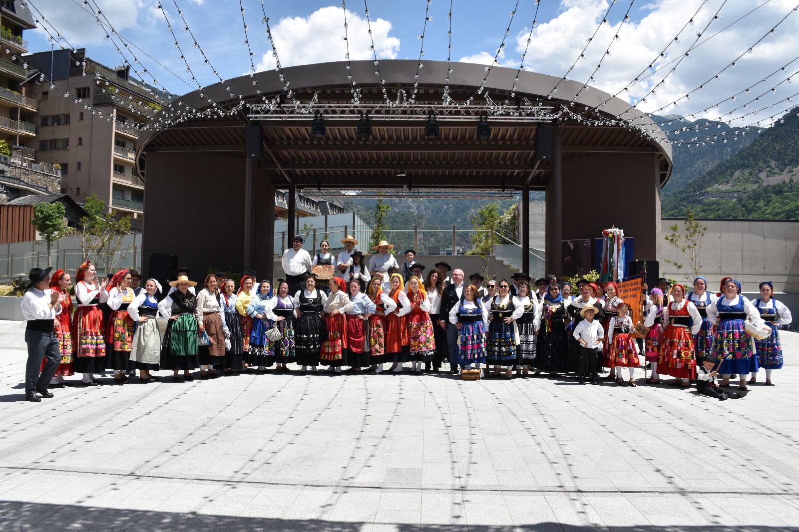 Grupo numeroso de pessoas com trajes tradicionais portugueses alinhadas em frente a um palco ao ar livre, durante o Festival de Folclore da Diáspora Portuguesa em Andorra.