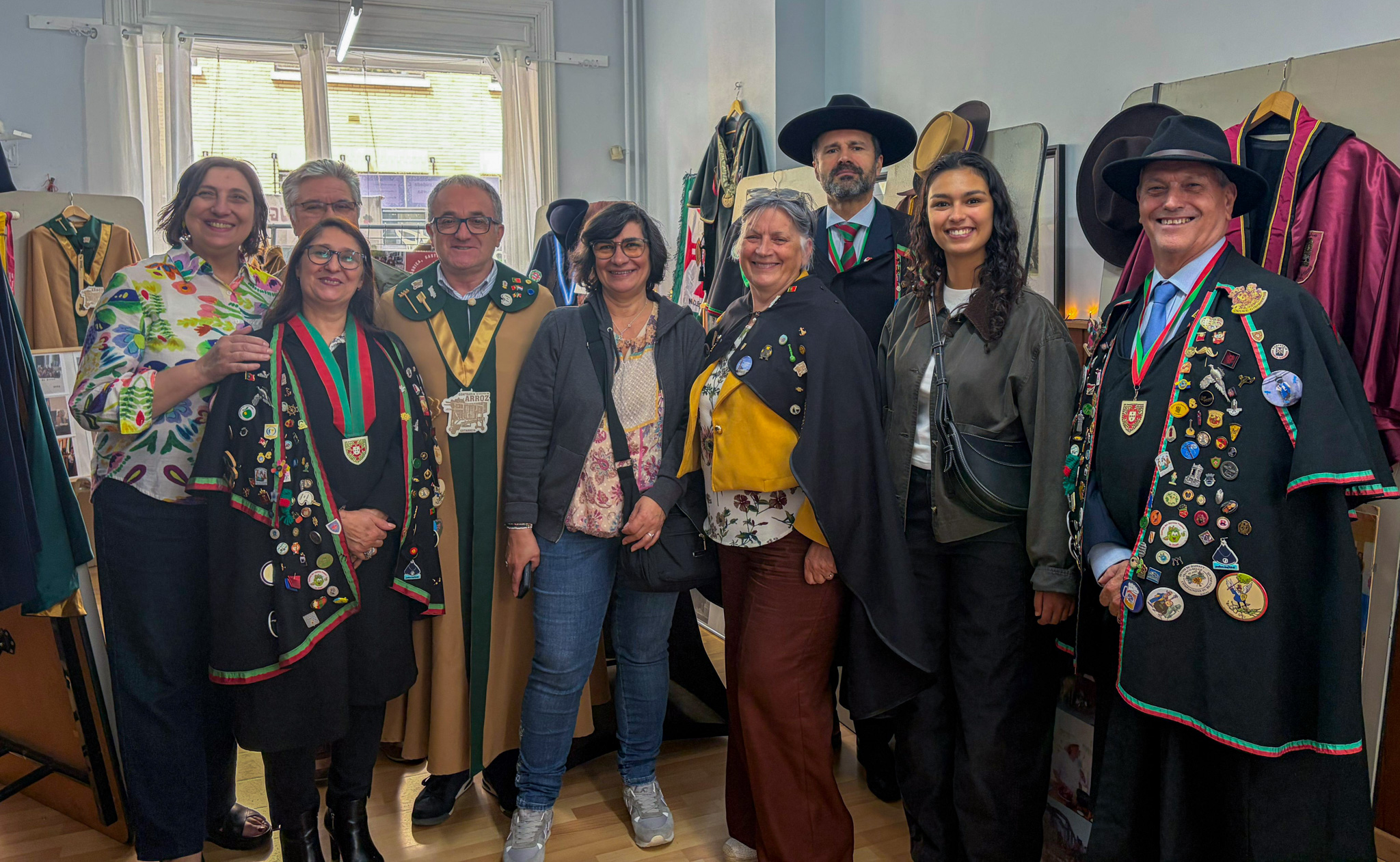 Grupo de pessoas, algumas com trajes tradicionais portugueses decorados com medalhas, reunidas num espaço interior durante um evento cultural dedicado às confrarias gastronómicas de Portugal na Bélgica.