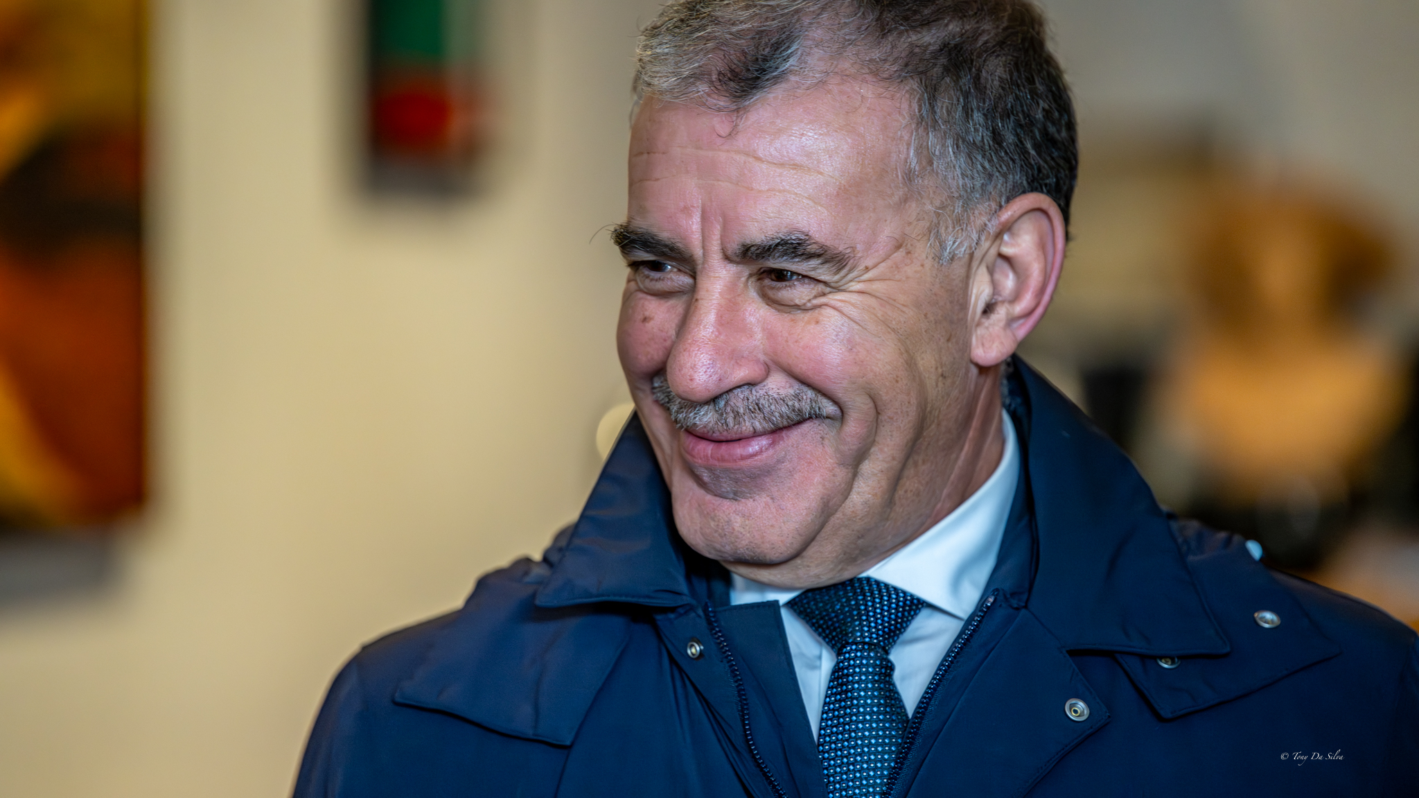 Homem de meia-idade, de fato e gravata, a sorrir num ambiente formal, sugerindo uma ocasião institucional.