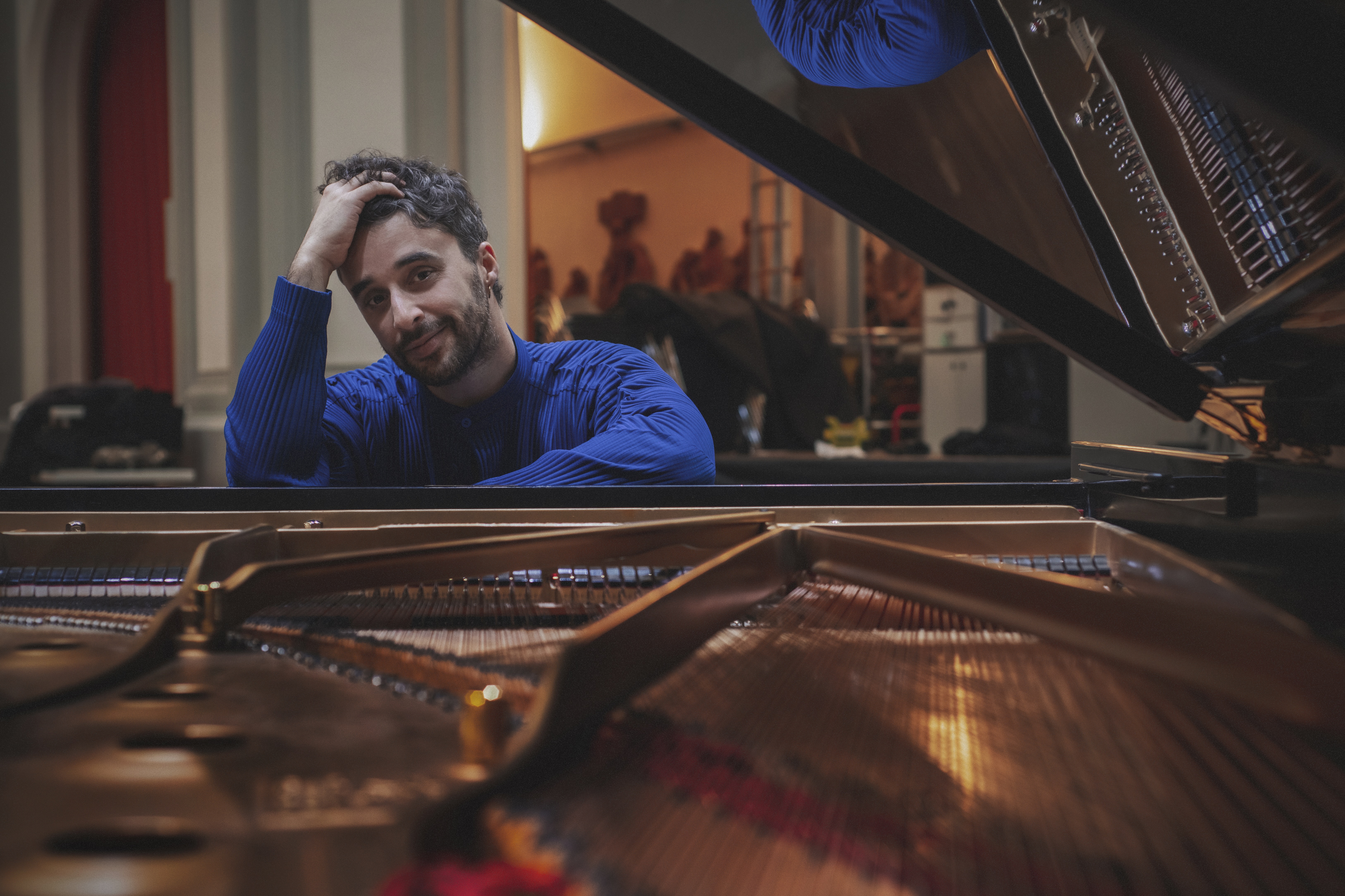 O pianista Raúl da Costa sentado junto a um piano de cauda aberto, com expressão descontraída, num ambiente interior de preparação para recital.