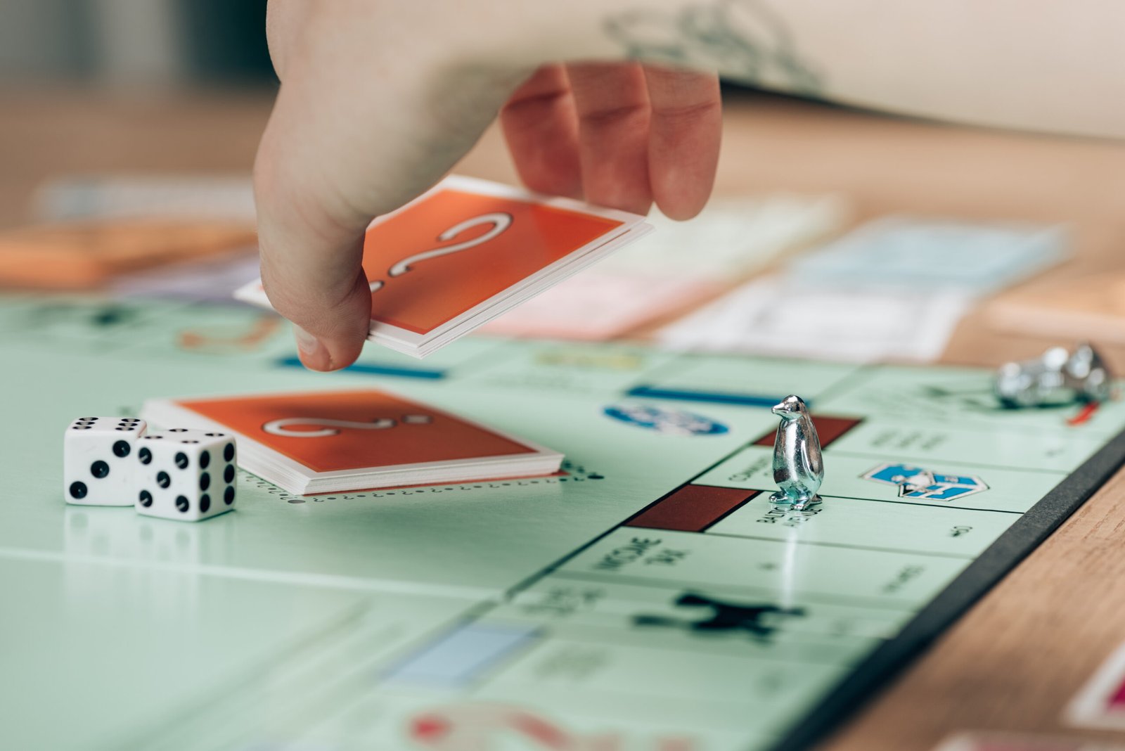 Mão a pegar numa carta de 'sorte' do jogo Monopoly, com dados e peças do tabuleiro visíveis, simbolizando o início de novas oportunidades e ligações, em referência ao evento 'Casa de Partida' em Bruxelas.