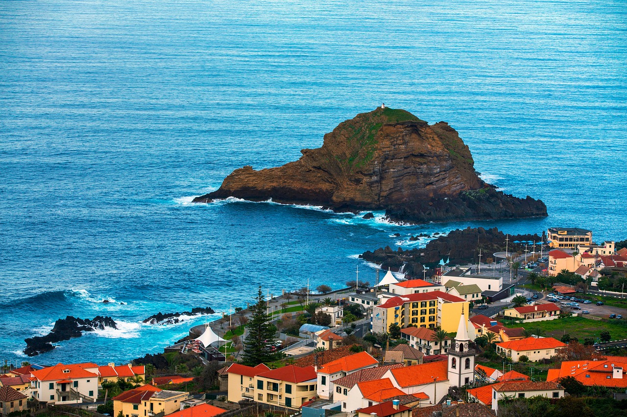 Vista de casas com telhados vermelhos junto ao mar e um ilhéu rochoso ao fundo, representando a paisagem da Madeira, local do curso para dirigentes associativos da diáspora portuguesa.