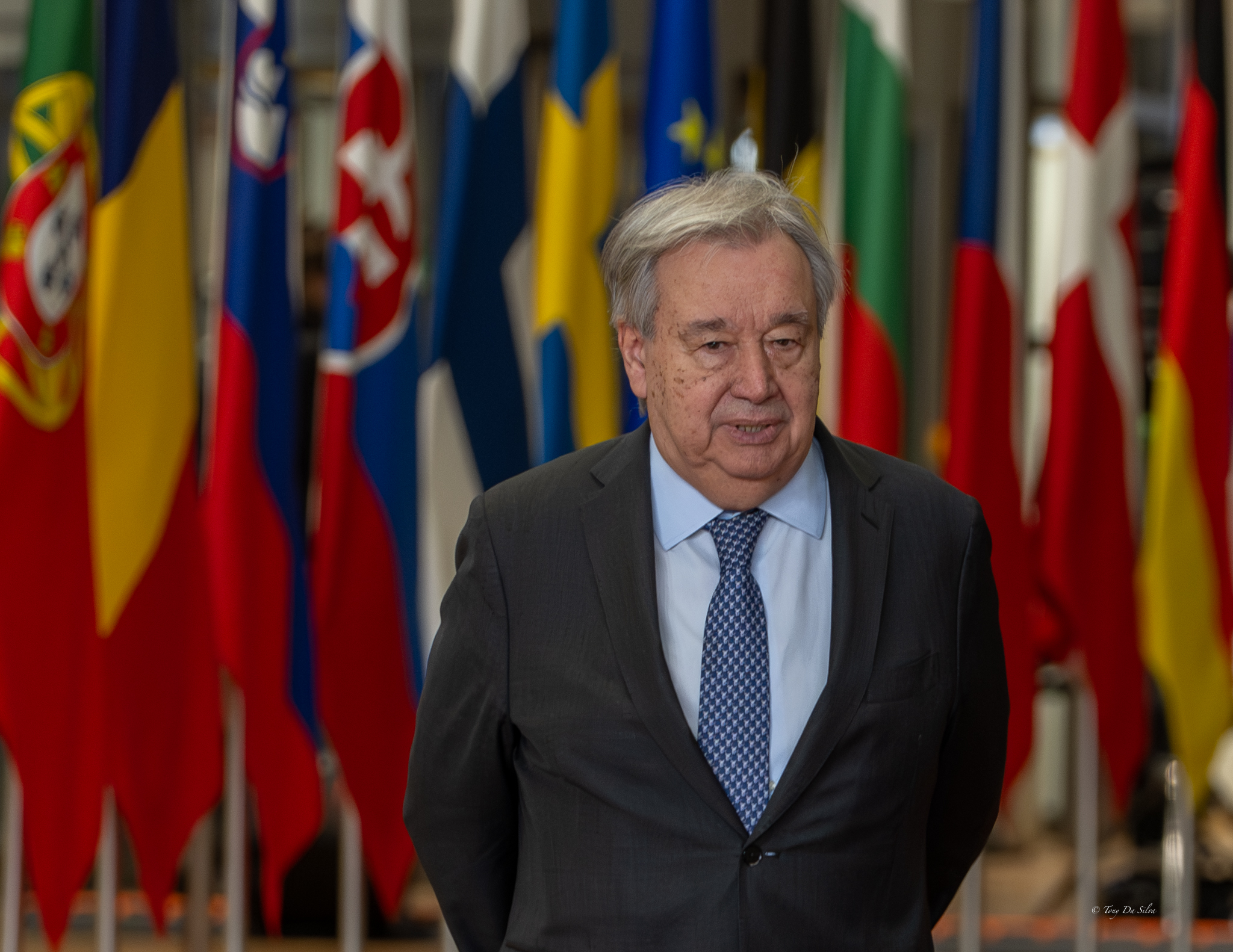 António Guterres, secretário-geral da ONU, em frente a várias bandeiras nacionais num evento internacional, simbolizando o contexto diplomático do seu apelo contra a islamofobia.