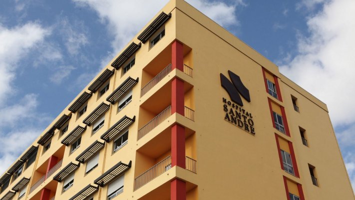 Fachada do Hospital de Santo André, em Leiria, com o logótipo visível na parede, sob um céu parcialmente nublado.