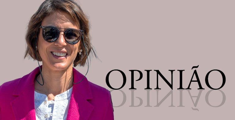 Pessoa sorridente com óculos de sol e casaco cor-de-rosa, ao lado da palavra 'OPINIÃO', ilustrando uma coluna de opinião sobre eleições no Benfica e política local.